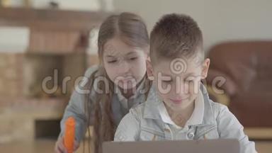 肖像可爱的小男孩坐在笔记本电脑上，小女孩，他的孪生妹妹在家里吹肥皂泡